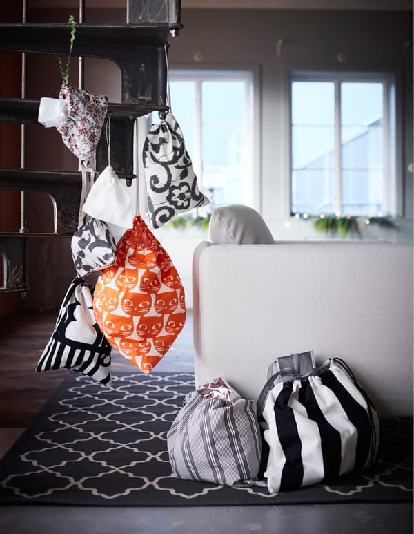 Sacs à cadeaux en textile ornés de différents motifs graphiques, certains attachés à un escalier en colimaçon, d'autres posés sur le sol.