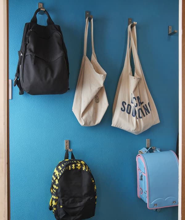 Sacs et sacs à dos suspendus à des crochets fixés à différentes hauteurs sur un mur bleu.