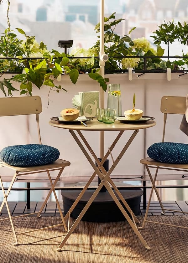 Sada vonkajšieho nábytku s rastlinami v pozadí - stôl a stoličky so sedákmi, dotvárajúce príjemnú atmosféru.