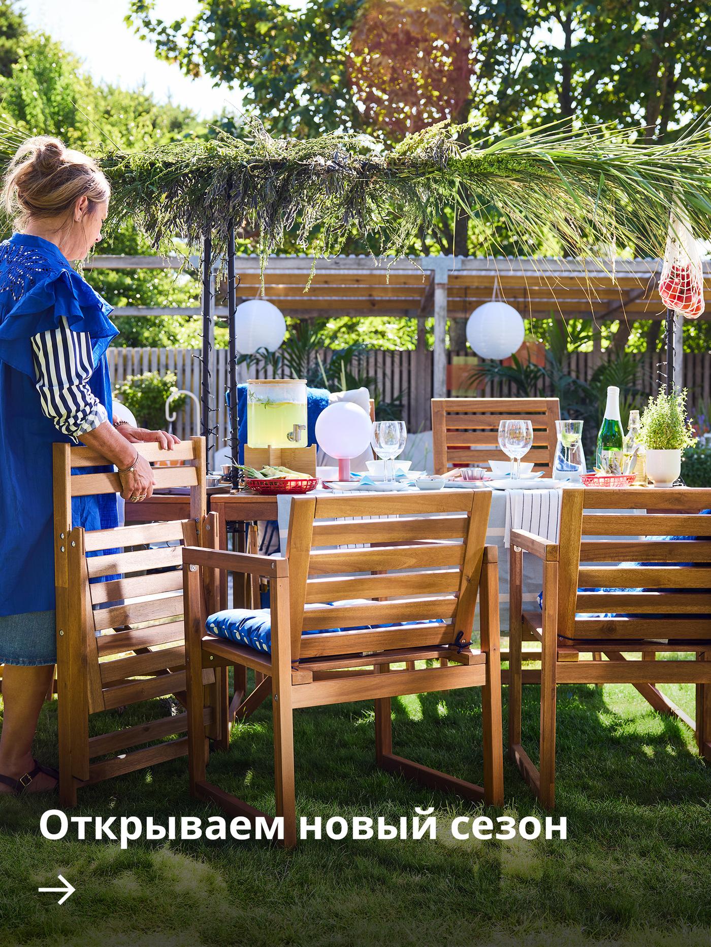 Садовая зона с чёрным угольным грилем GRILLSKÄR и деревянными модулями уличной кухни NÄMMARÖ под перголой.