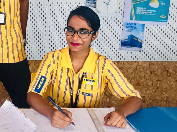 Safia Begum, a co-worker at IKEA India, sitting while writing something on paper and smiling.