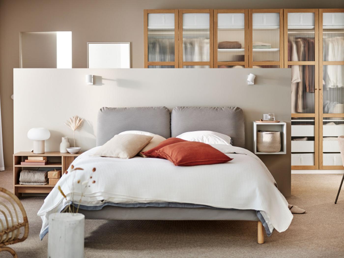 SAGESUND gestoffeerd bed in Diseröd bruin/Luröy, opgemaakt in het wit en met rode kussens erop, in een grote, luchtige slaapkamer.