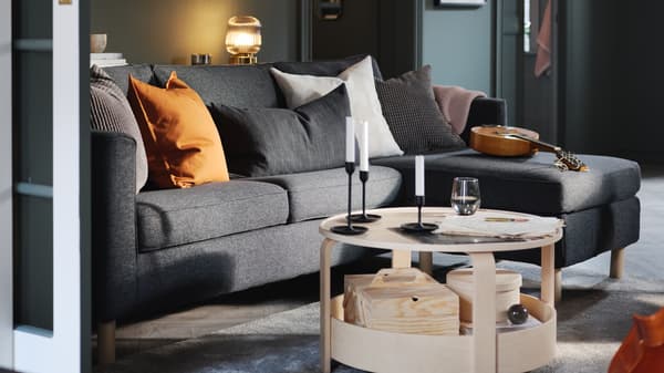 Sala com parede verde, sofá de três lugares com chaise longue PÄRUP em cinzento escuro e mesa de centro BORGEBY em bétula.