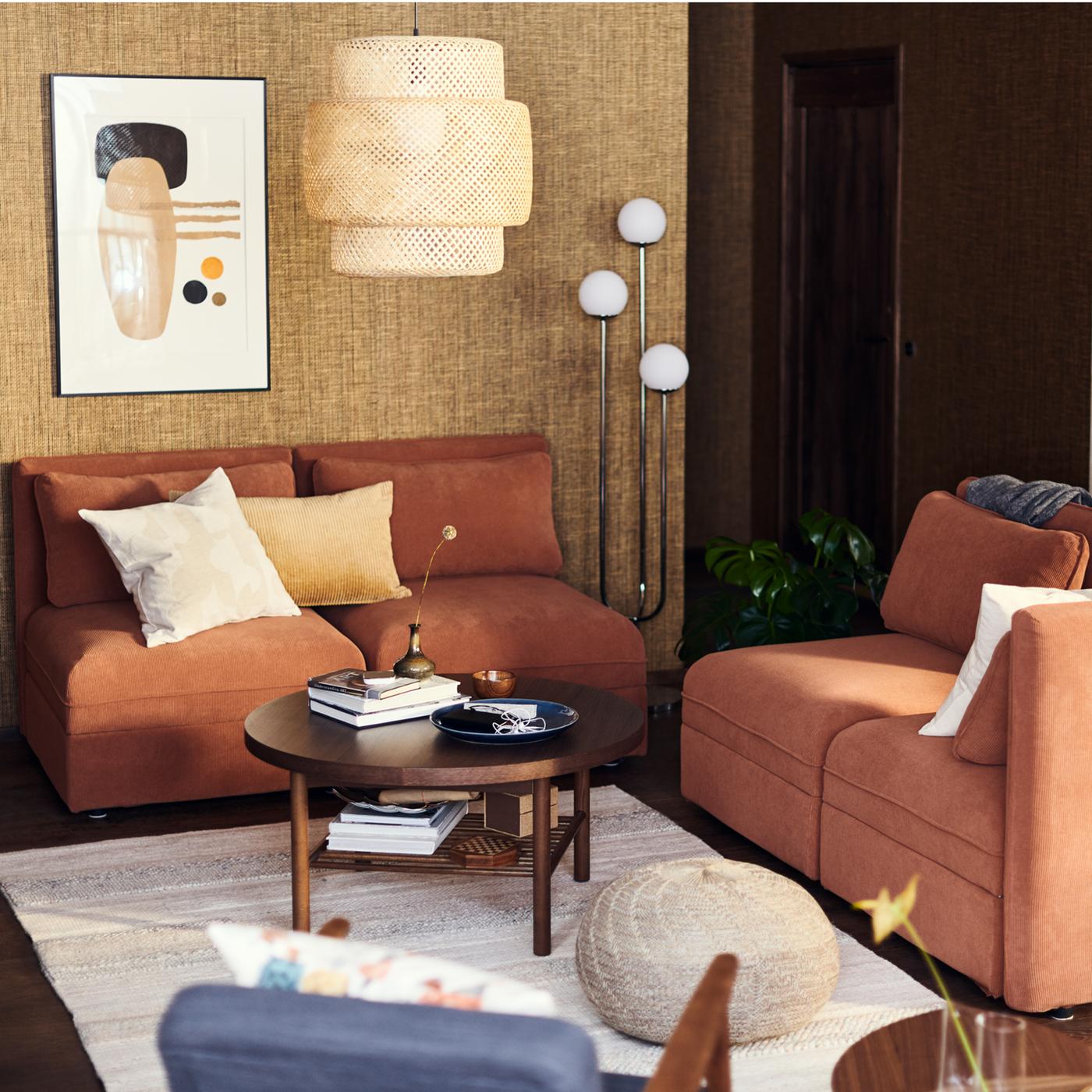 Sala com sofás modulares VALLENTUNA em cor de ferrugem com um candeeiro suspenso SINNERLIG em bambu por cima.