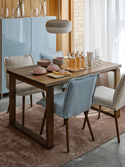 Sala da pranzo con un tavolo MÖRBYLÅNGA e sedie. Sul tavolo, ci sono diverse stoviglie e sopra una lampada a sospensione BLÅSVERK. A lato, una porta finestra con tenda bianca da cui entra luce.