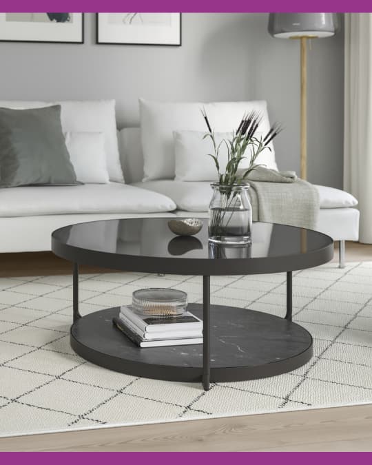 Sala de estar con sofá claro y mesa de centro redonda negra con repisa inferior y decoración simple.