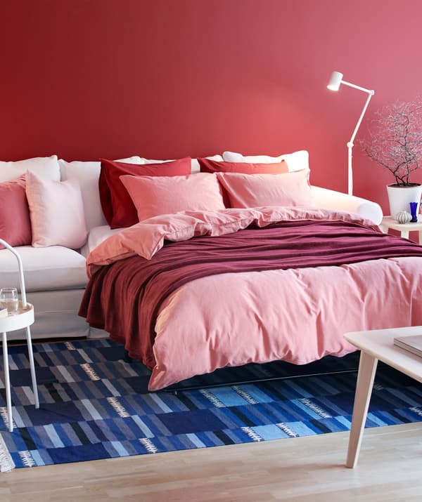 Sala de estar con sofá GRÖNLID estendido para converterse nunha cama de matrimonio, ben feita, con varias capas de téxtiles e coxíns moles.