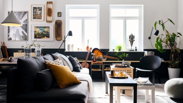 Sala de estar cun sofá SÖDERHAMN gris escuro, cadros, mesas niño LACK en branco e negro, e unha lámpada de lectura SKURUP negra.