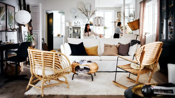 Sala de estilo rústico em tons de branco com duas mulheres atrás de um sofá BACKSÄLEN em branco, à frente de um tapete e duas poltronas.