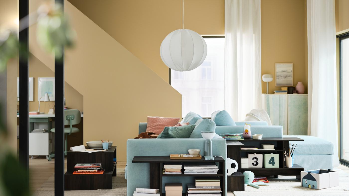 Sala elegante com paredes em amarelo e sofá-cama de 3 lugares VIMLE em azul claro, costas com costas com uma chaise longue VIMLE.