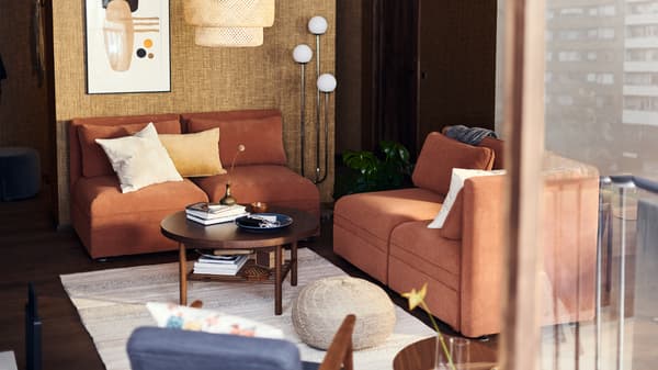 Sala em tons neutros com dois sofás VALLENTUNA em cor de ferrugem e uma mesa de centro redonda. No chão, há um tapete em creme.
