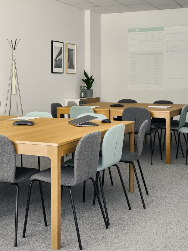 Sala konferencyjna z drewnianymi stołami i różnymi krzesłami.