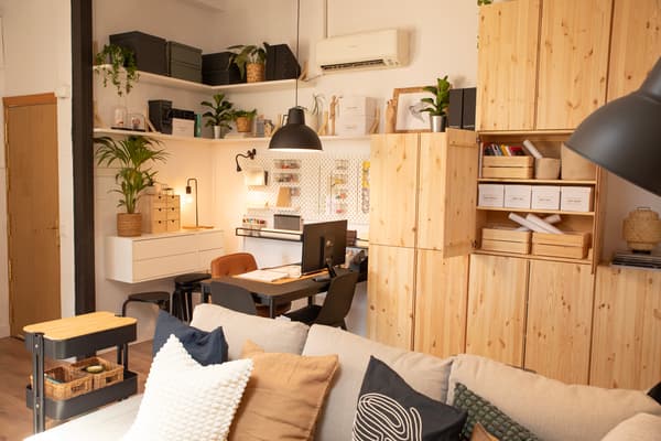 Sala reformada amb una prestatgeria de fusta, un sofà, coixins, un carretó, lleixes, un escriptori, una cadira i objectes de decoració. 