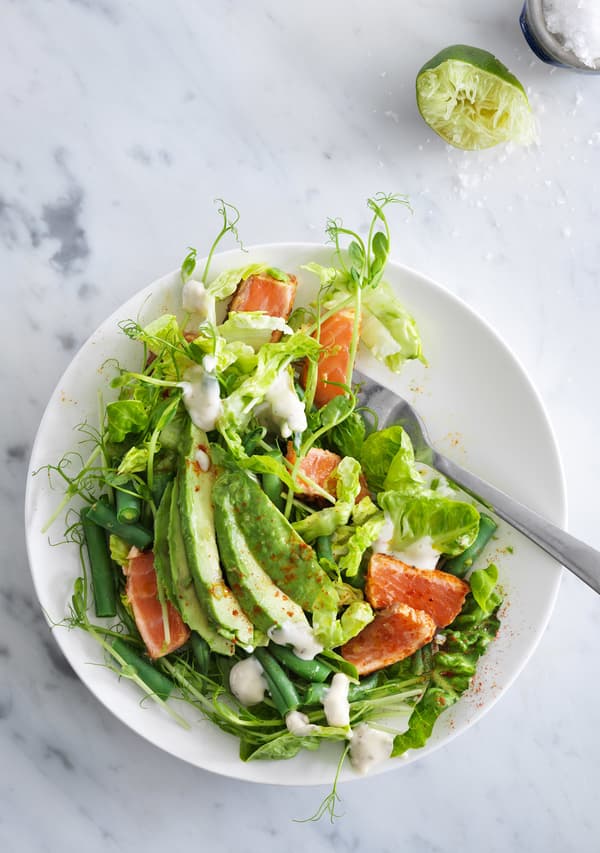 Salad with spicy salmon and avocado served in a white stoneware bowl, seen from above.