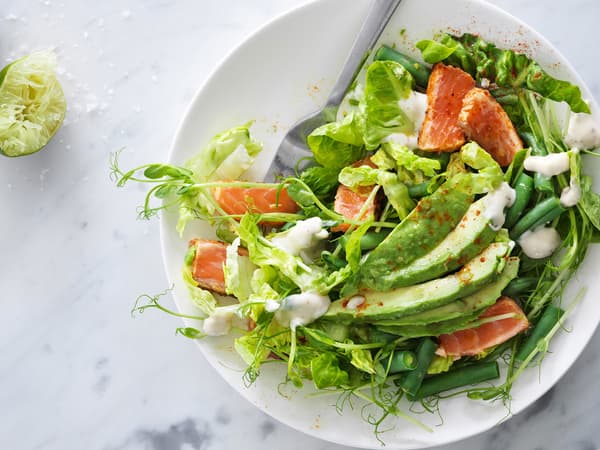 Salad with spicy salmon and avocado served in a white stoneware bowl, seen from above.