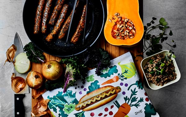 Salchichas nunha tixola, leitugas e hortalizas, e un envase de bocadillos de salchichas nunha táboa de madeira.