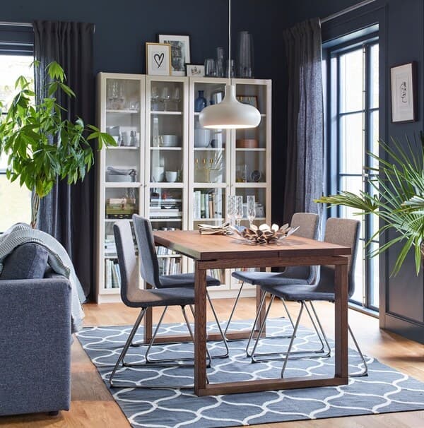 Salle à manger avec une table en bois, quatre chaises rembourées et une vitrine avec de la vaisselle rangée à l'intérieur.
