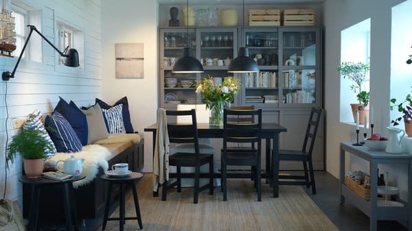 Salle à manger avec une table et des chaises noires, un tapis en jute, des suspensions noires et une combinaison de rangement aux portes coulissantes.