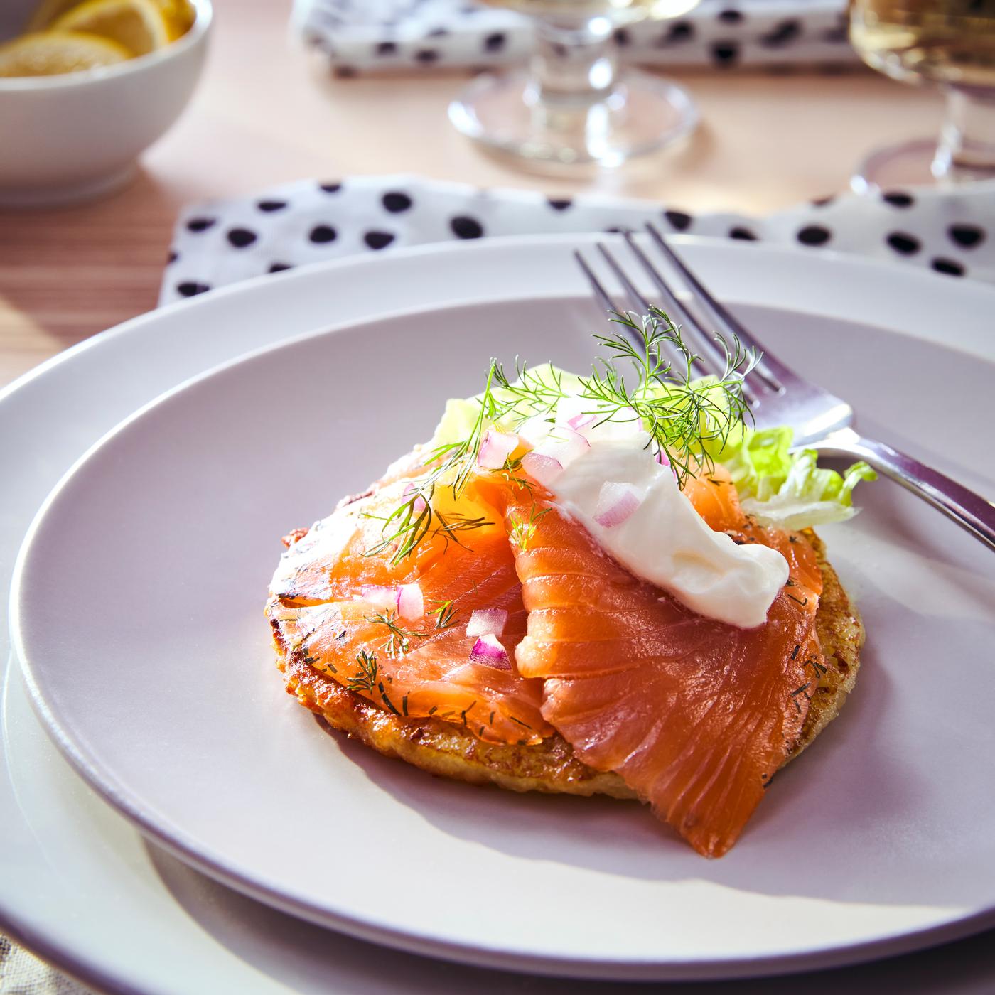 Salmão curado fumado a frio SJÖRAPPORT, com certificação ASC, preparado com endro, cebola picada e molho, num prato em branco ao lado de um garfo.