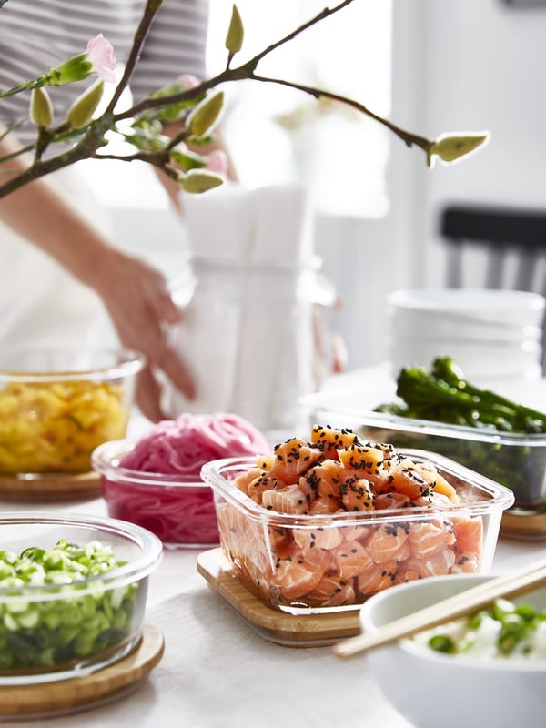Salmon and vegetables neatly stored in IKEA 365+ glass food containers on a bright dining table, with spring branches in the background.