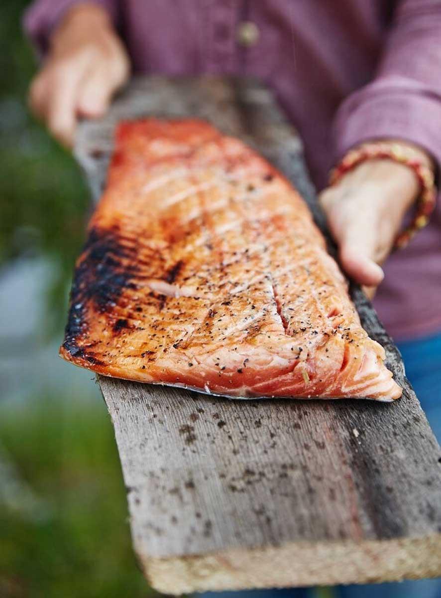 Salmone cotto alla brace; una persona lo sta servendo su un asse di legno.