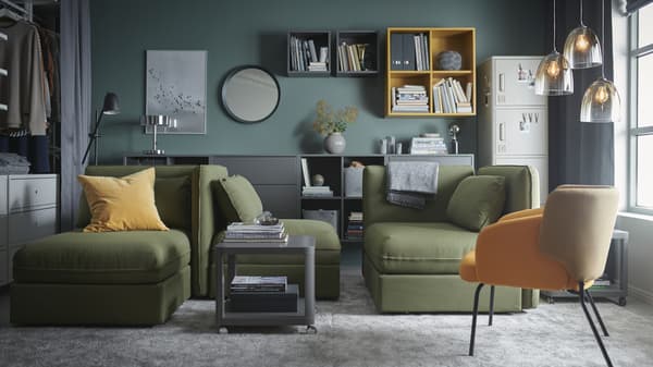 Salon avec canapés convertibles modulaires VALLENTUNA en vert, grands tapis gris, armoires en gris et jaune, et suspensions en verre.
