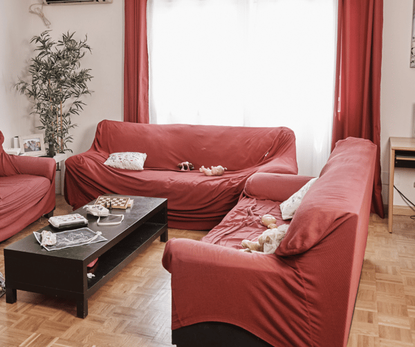 Salón con 3 sofás con fundas rojas, mesa y juguetes por el suelo.