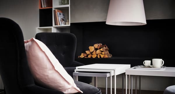 Salón con sillones negros y dos juegos de nidos de mesas de centro, con troncos para encender la chimenea al fondo.