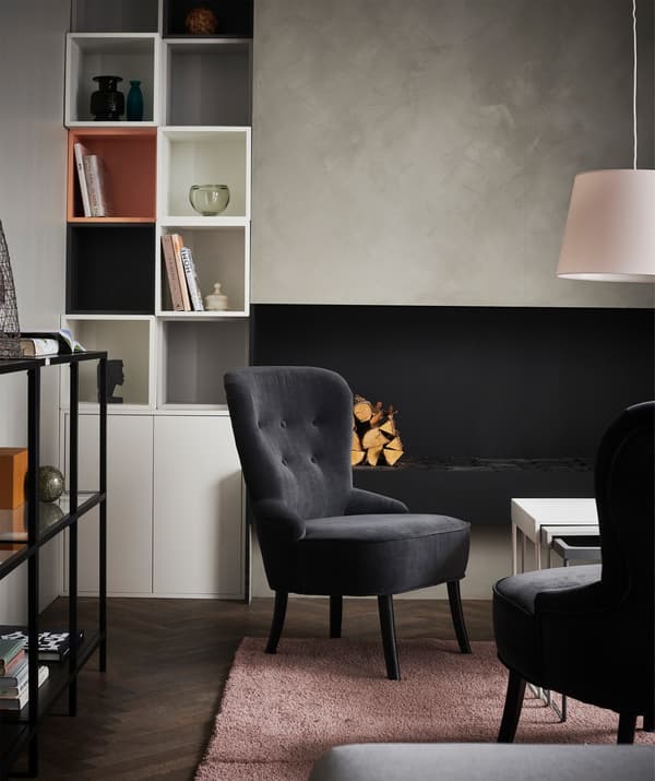 Salón con sillones negros y una alfombra rosa, rodeados de un sistema de almacenaje con objetos expuestos en las paredes.
