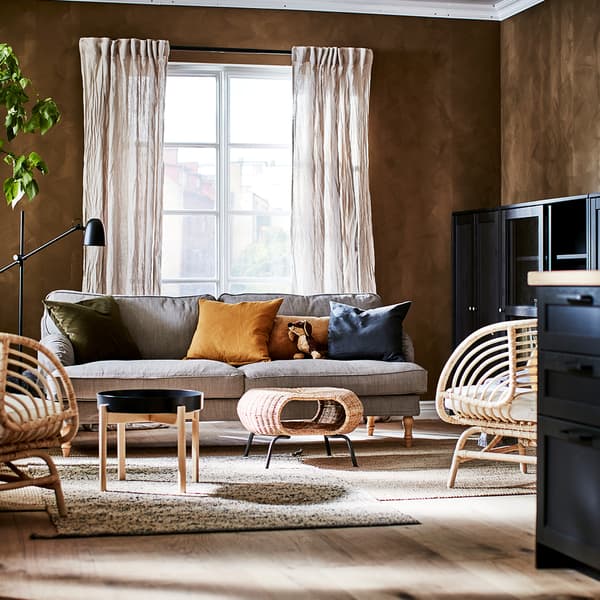 Salón de estilo escandinavo tradicional de IKEA con sillones de mimbre, un reposapiés de ratán en el centro junto a una mesa de metal y madera.