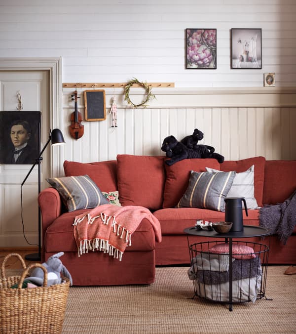 Salón de IKEA de estilo escandinavo tradicional con un sofá rojo, una mesa de centro negra redonda, una lámpara de pie negra y cojines en tono denim y gris.
