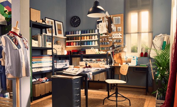 Same office transformed into a tailoring workshop, with shelving to store fabrics and spools of thread, and a desk and chair in the middle.