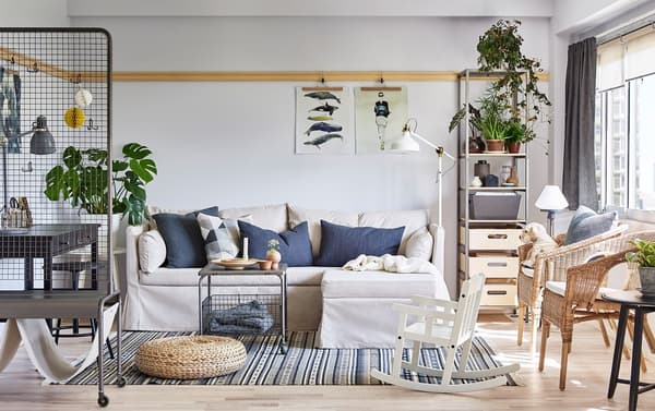 SANDBACKEN corner sofa bed in Lofallet beige cover with blue cushions in a bright sitting room with rattan furniture.