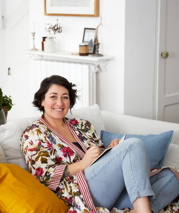 Sarah นั่งอยู่บนโซฟาสีขาวในห้องที่ตกแต่งด้วยสีขาว