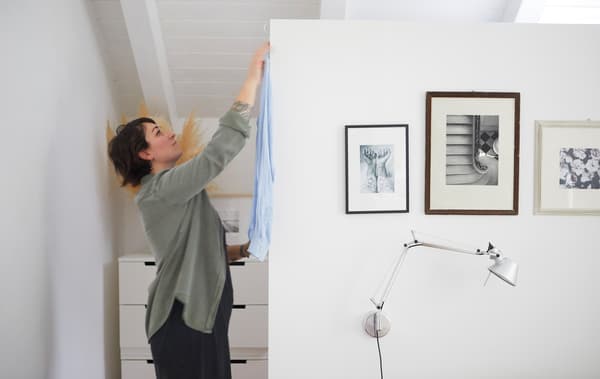 Sarah appende una camicia dietro a una parete bianca decorata con fotografie in bianco e nero - IKEA
