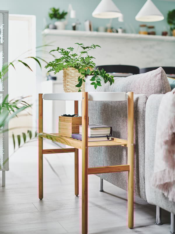 ต้นไม้กระถางขนาดเล็กสองต้นและที่เก็บของสีอ่อนวางอยู่บนที่วางกระถางต้นไม้ SATSUMAS/ซาทซูมาส ที่อยู่ถัดจากโซฟาห้องนั่งเล่น