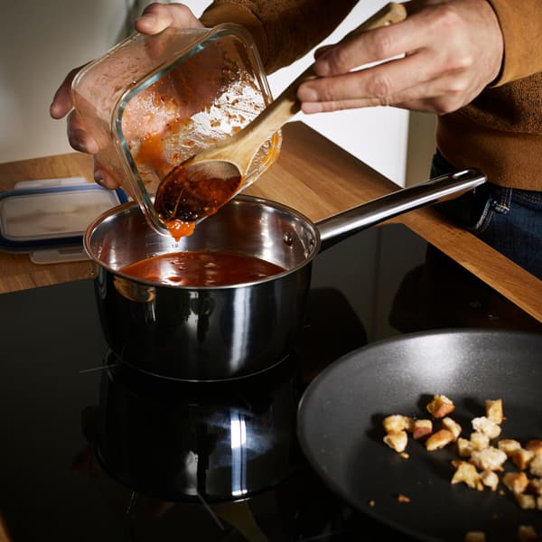Sauce tomate versée d'un récipient IKEA 365 dans une casserole sur une plaque à induction.