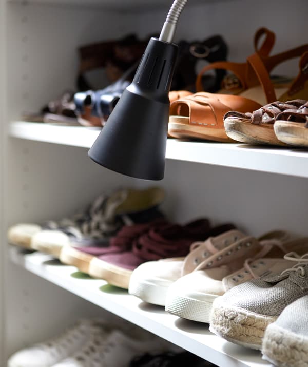 Scarpe disposte in fila su una mensola e una lampada da lavoro nera – IKEA