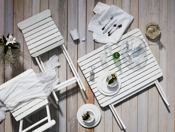 Schematisches Arrangement eines Dinnersets, u. a. mit MÄLARÖ Stuhl/außen faltbar weiß, ergänzt durch einen Tisch und Textilien in Weiß.