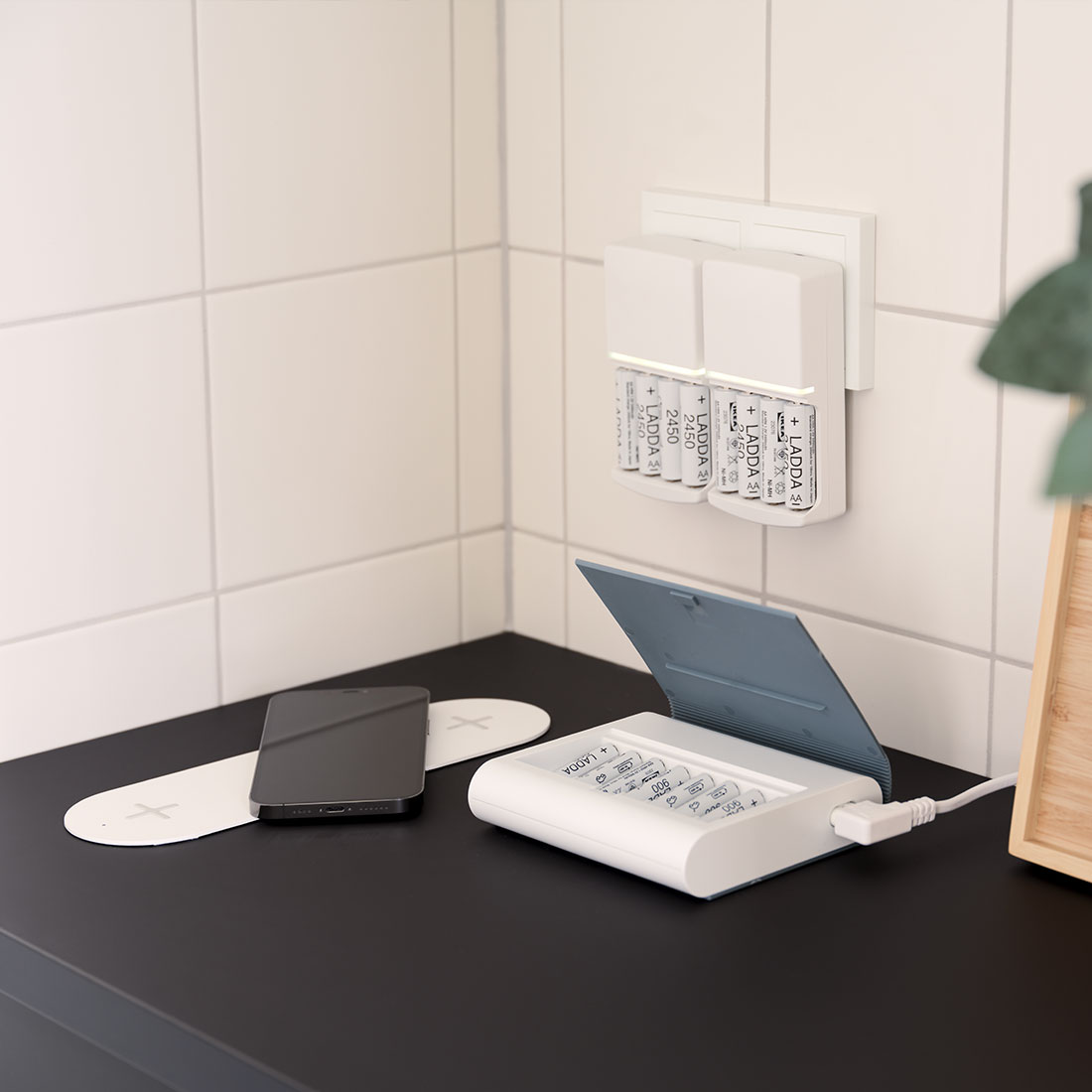 Schwarze Küche mit weißen Wandkacheln. Auf der Arbeitsplatte liegt ein Ladegerät für ein Smartphone, ein Akku und eine Batterieladestation an der Wand.