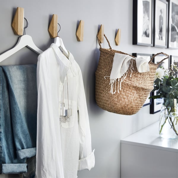 Ściana z pięcioma bambusowymi haczykami IKEA SKUGGIS używanymi do wieszania ubrań i kosza.
