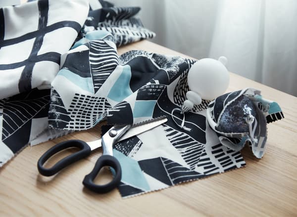 Scissors and graphic patterned fabric on a table, used to prepare small snippets of fabric to wrap holiday decorations.