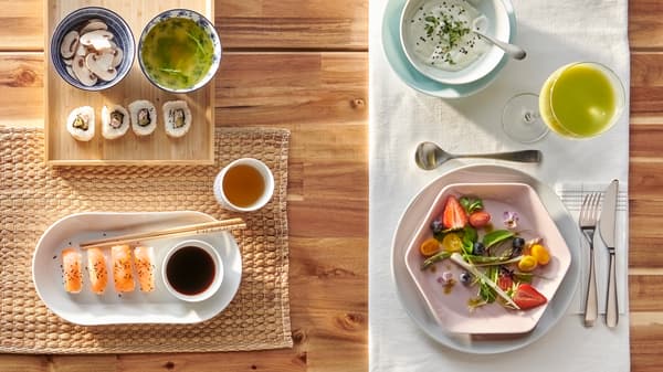 Sebuah meja disediakan dalam dua cara, satu untuk sushi dalam pinggan bujur berwarna putih dan satu lagi untuk salad dalam pinggan heksagon berwarna merah jambu.