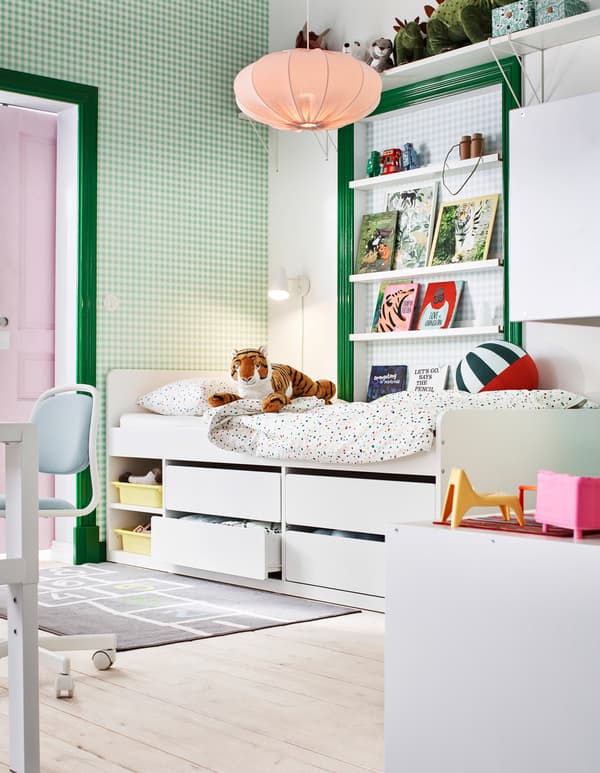 Secção de um quarto de criança num esquema de cores em branco e verde, com livros, brinquedos e uma estrutura de cama com arrumação em baixo.