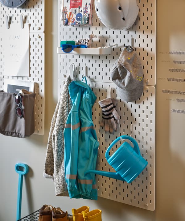 Secção de uma parede da entrada equipada com placares SKÅDIS com brinquedos, peças de roupa e acessórios colocados a diferentes alturas.