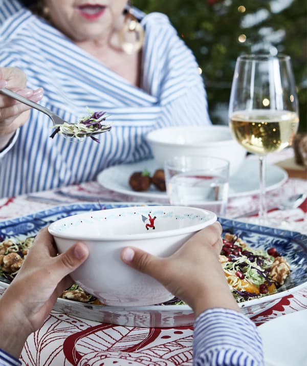 Sección de mesa de Nadal con pratos e vasos cheos. Unha persoa máis vella sérvelle comida a un neno nun cunco.