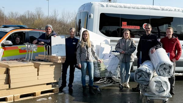 Sechs Personen stehen auf dem Parkplatz von IKEA Würzburg zwischen zwei Johanniter‑Fahrzeugen und mehreren Einkaufswagen sowie Paletten voller flach verpackter Möbel und Einrichtungsgegenständen. Die Gruppe wurde während einer Spendenaktion von IKEA Würzburg an die Johanniter-Unfall-Hilfe e.V. in Unterfranken fotografiert, im Hintergrund sind ein weißer Johanniter‑Transporter und ein gelb‑rot markiertes Einsatzfahrzeug der Johanniter zu sehen.
