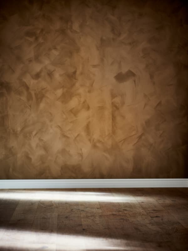 Section of an empty room with wooden floor and the wall painted in a rich, brown tone with a matte suede finish.