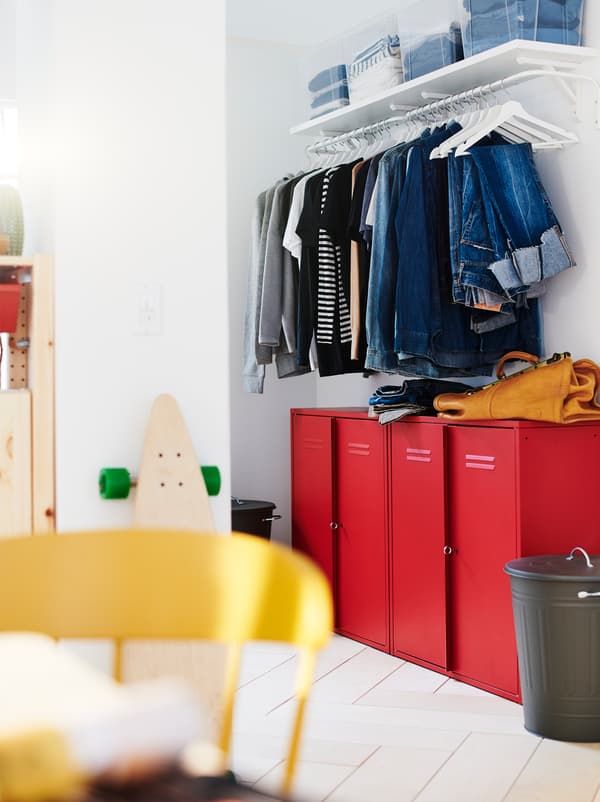 Secțiune a unui perete cu o combinație de dulap de haine și soluție de depozitare pentru hol: copuri IVAR roșii sub un rând de haine pe umerașe agățate pe un suport.