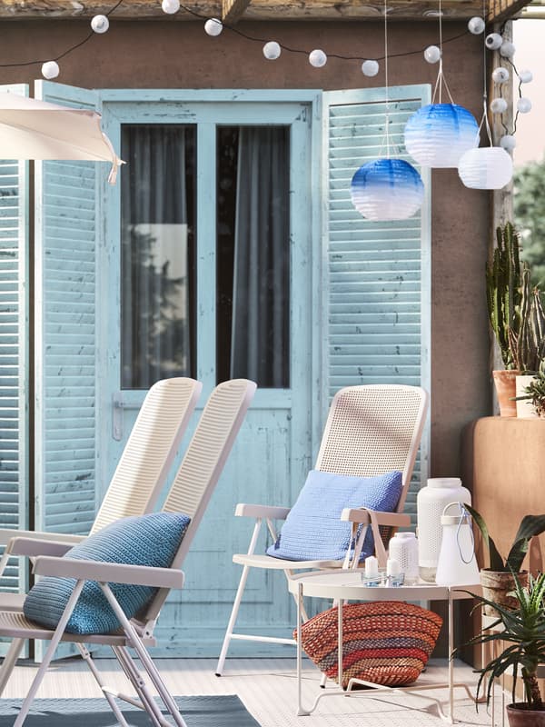 Sedie da esterno bianche con cuscini azzurri accanto ad un tavolino basso bianco. Sullo sfondo una portafinestra con ante azzure.